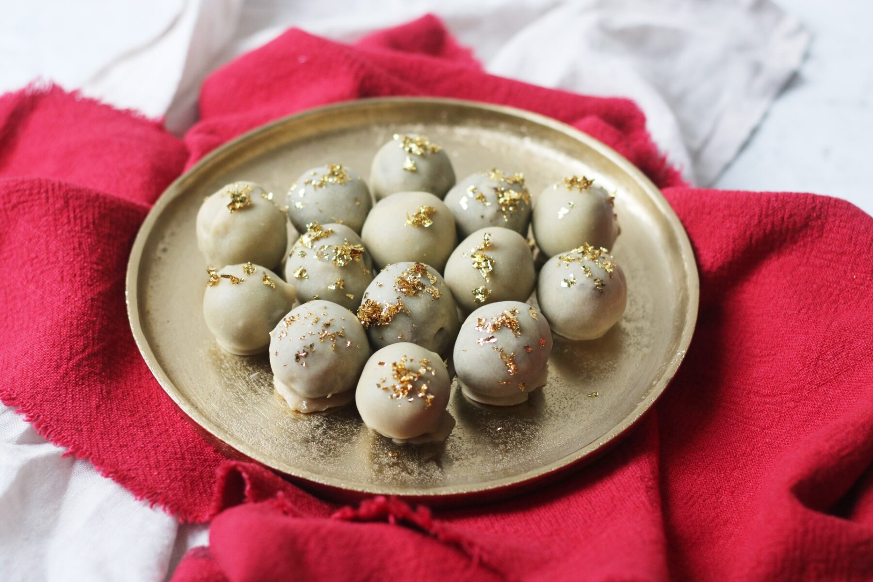 Vegan white chocolate and champagne truffles topped with gold leaf on a gold plate and red napkin.