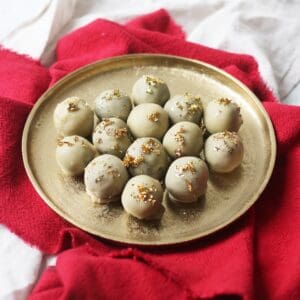 Vegan white chocolate and champagne truffles topped with gold leaf on a gold plate and red napkin.