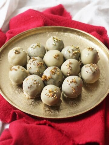 Vegan white chocolate and champagne truffles topped with gold leaf on a gold plate and red napkin.