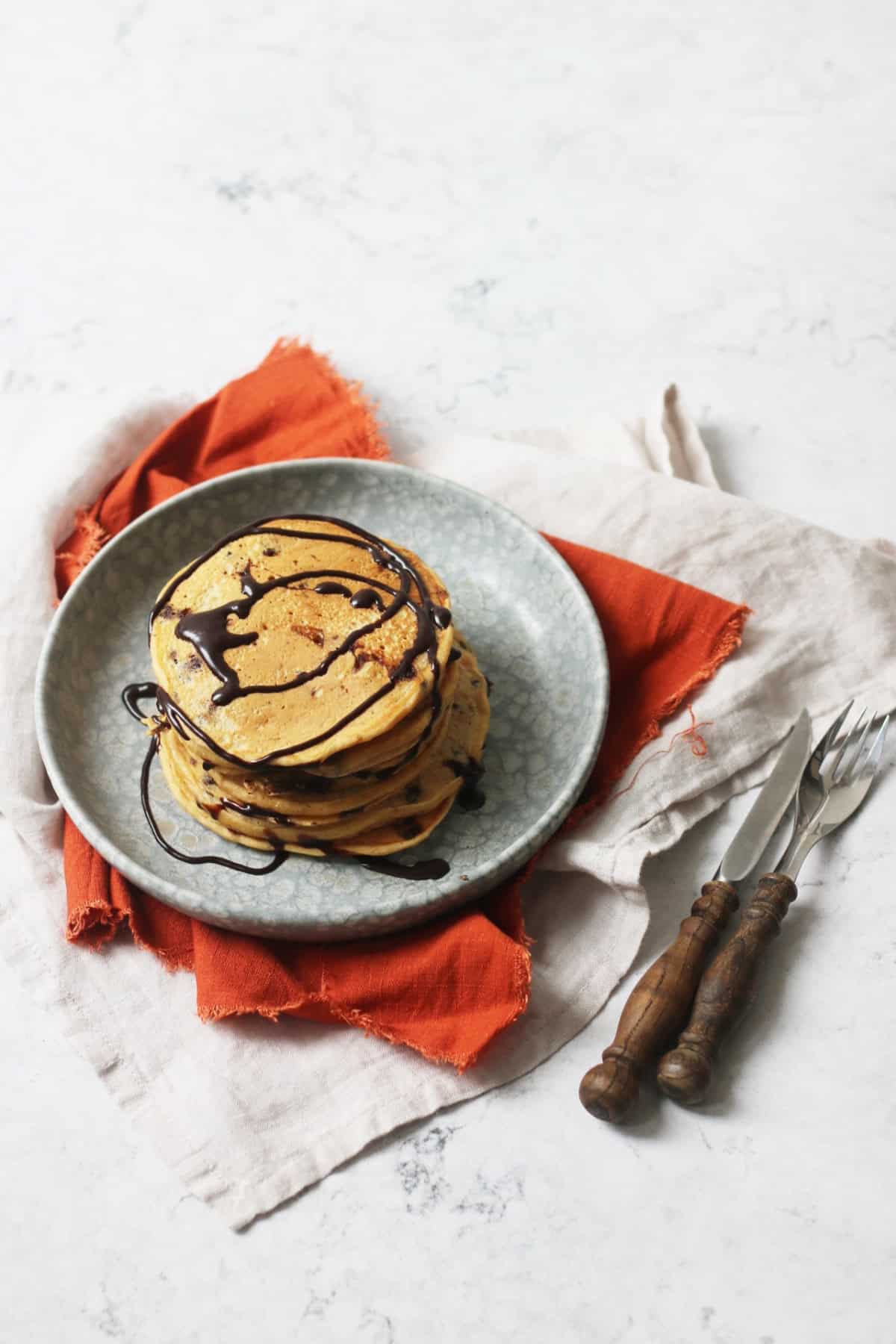 A stack of Vegan Sweet Potato Pancakes with chocolate sauce