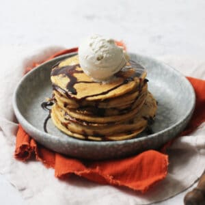 A stack of Vegan Sweet Potato Pancakes with chocolate sauce