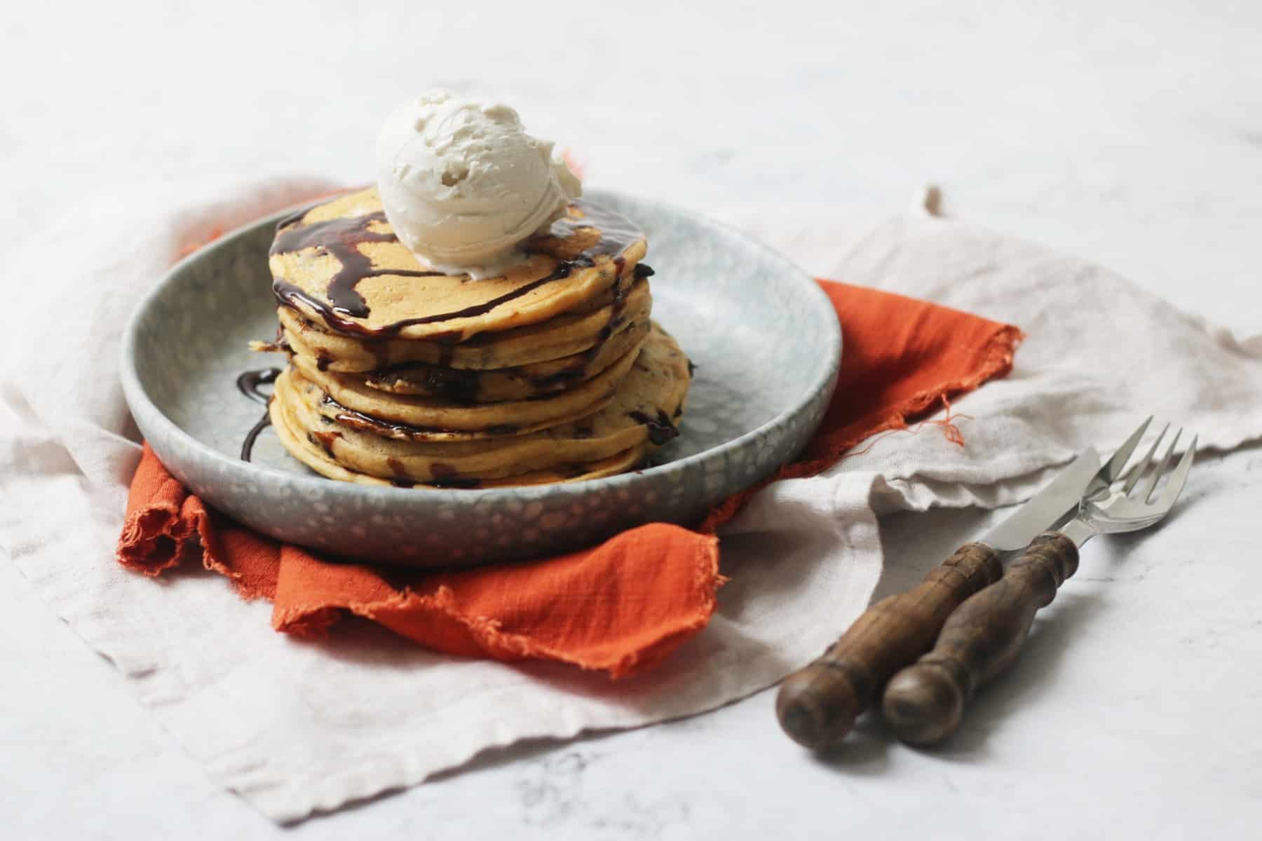 A stack of Vegan Sweet Potato Pancakes with chocolate sauce and a knife and fork