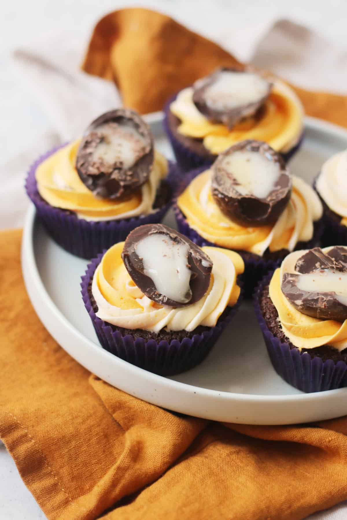 Vegan Creme Egg Cupcakes on a plate sat on top of a yellow napkin