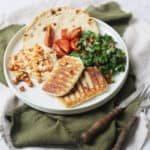 A plate topped with a flatbread, hummus and chickpeas, tabbouleh, sun dried tomatoes and vegan halloumi that has been grilled