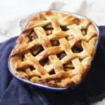 A baked vegan apple and blackberry pie with a lattice top in an oval pie tin