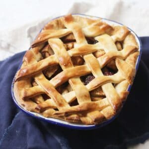 A baked vegan apple and blackberry pie with a lattice top in an oval pie tin