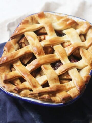 A baked vegan apple and blackberry pie with a lattice top in an oval pie tin