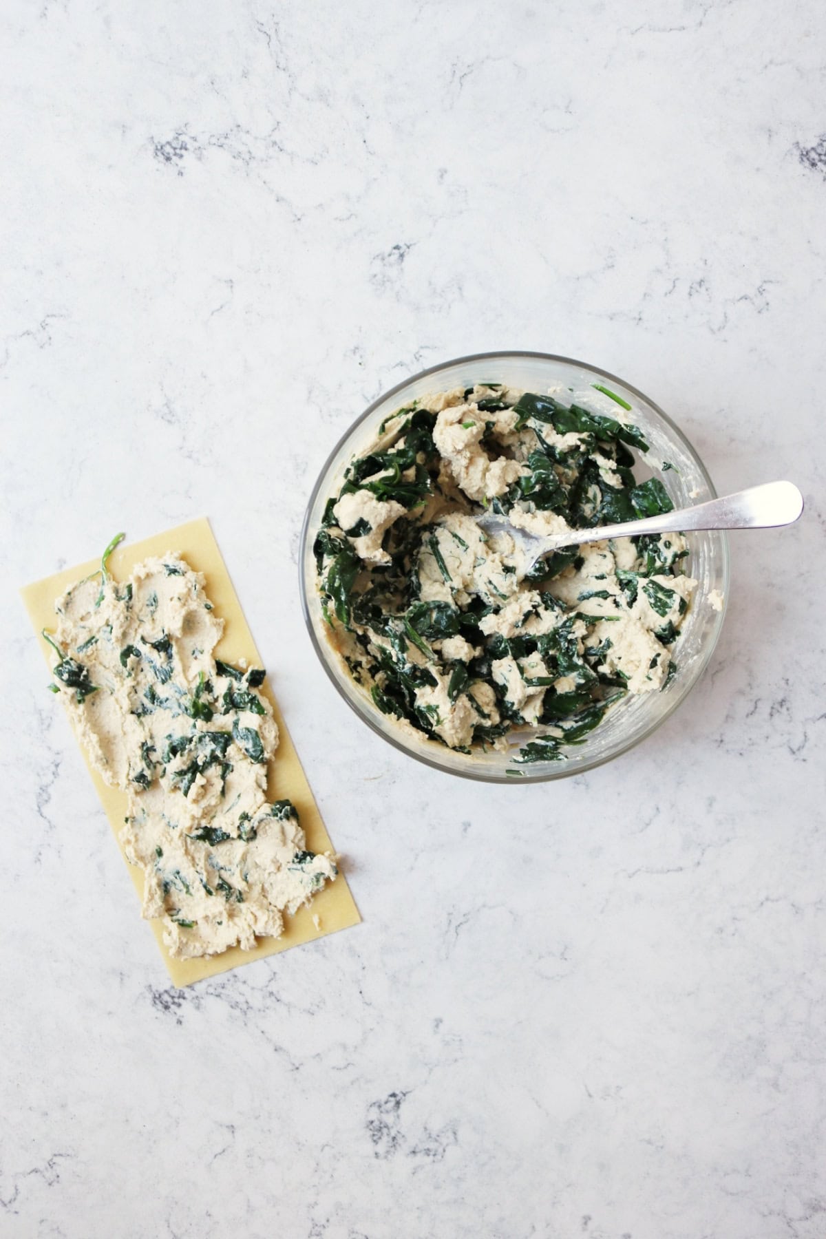 On the left is a fresh lasagne sheet with spinach and vegan ricotta spread on top and on the right is the bowl of spinach and vegan ricotta