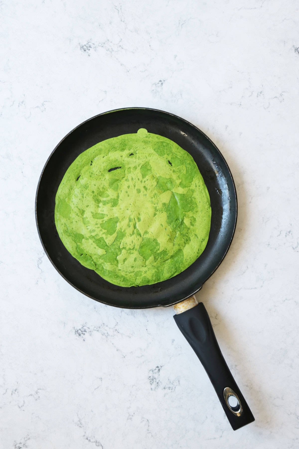 A spinach crêpe cooking in a crêpe pan