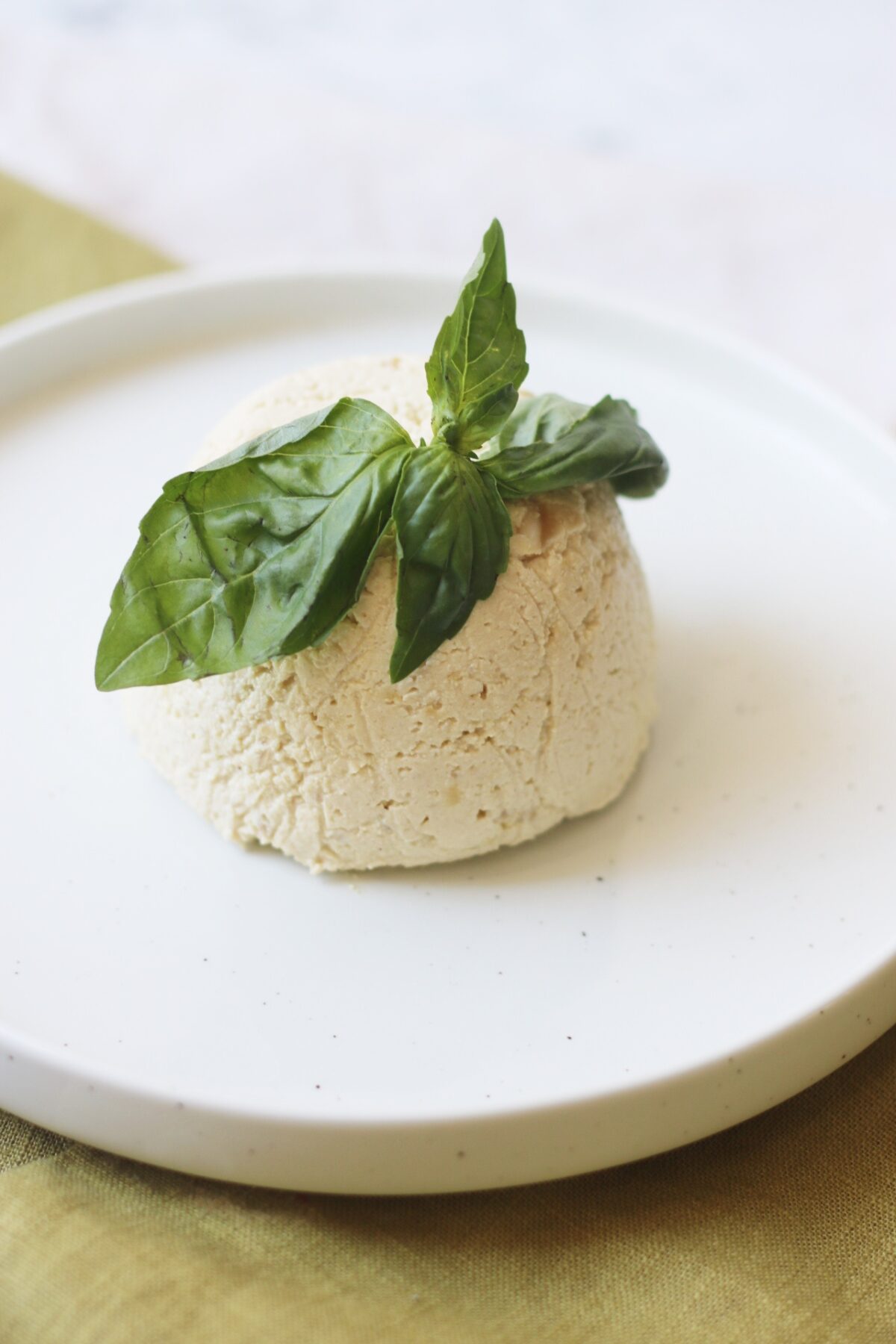 A dome of vegan ricotta on a plate topped with fresh basil