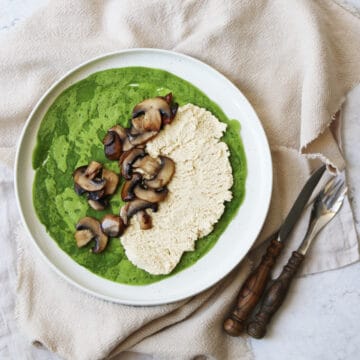 A spinach crêpe on a plate topped with vegan ricotta and cooked mushrooms