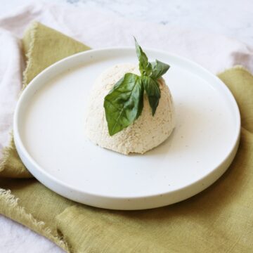 A dome of vegan ricotta on a plate topped with fresh basil