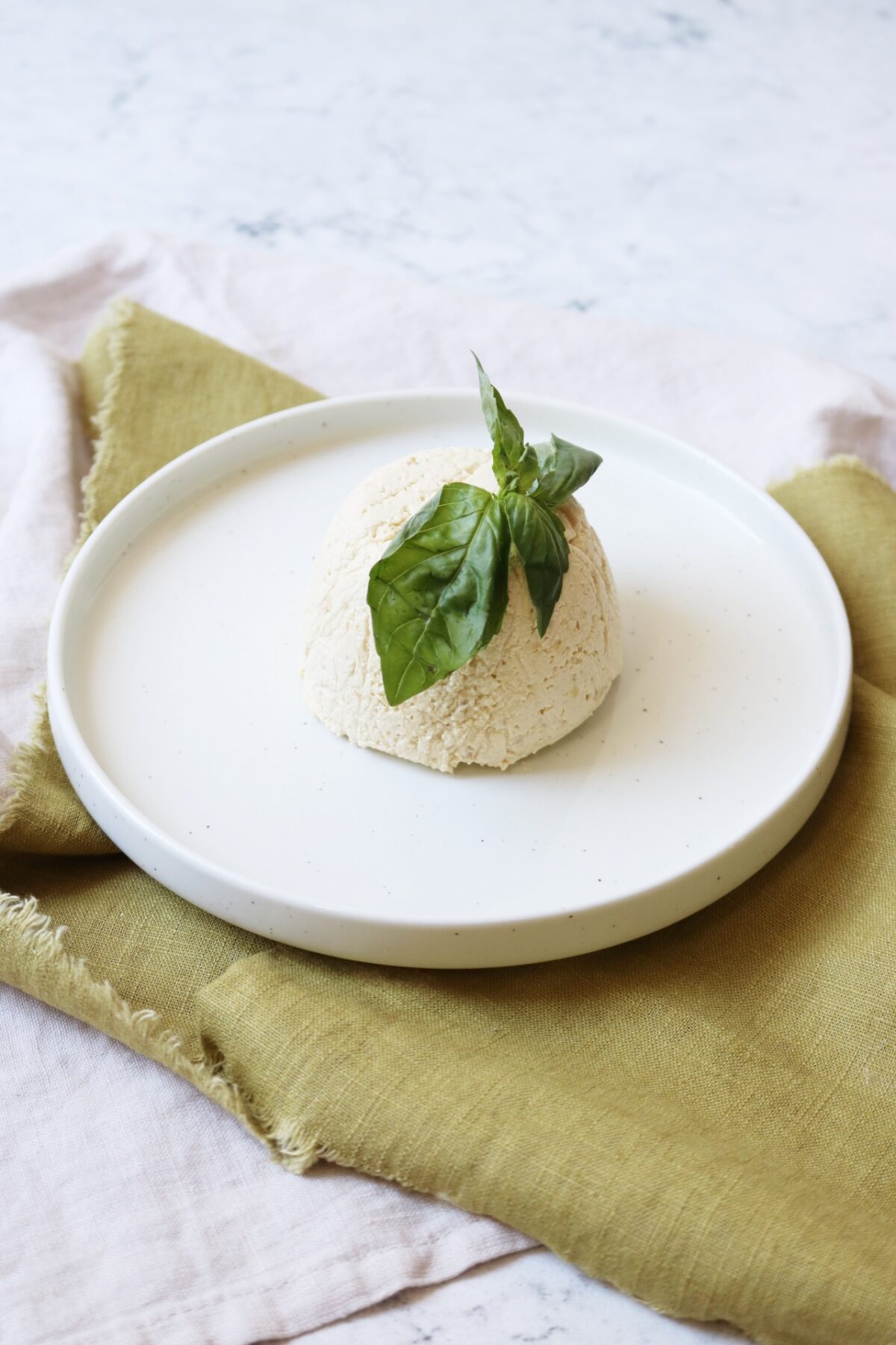 A dome of vegan ricotta on a plate topped with fresh basil