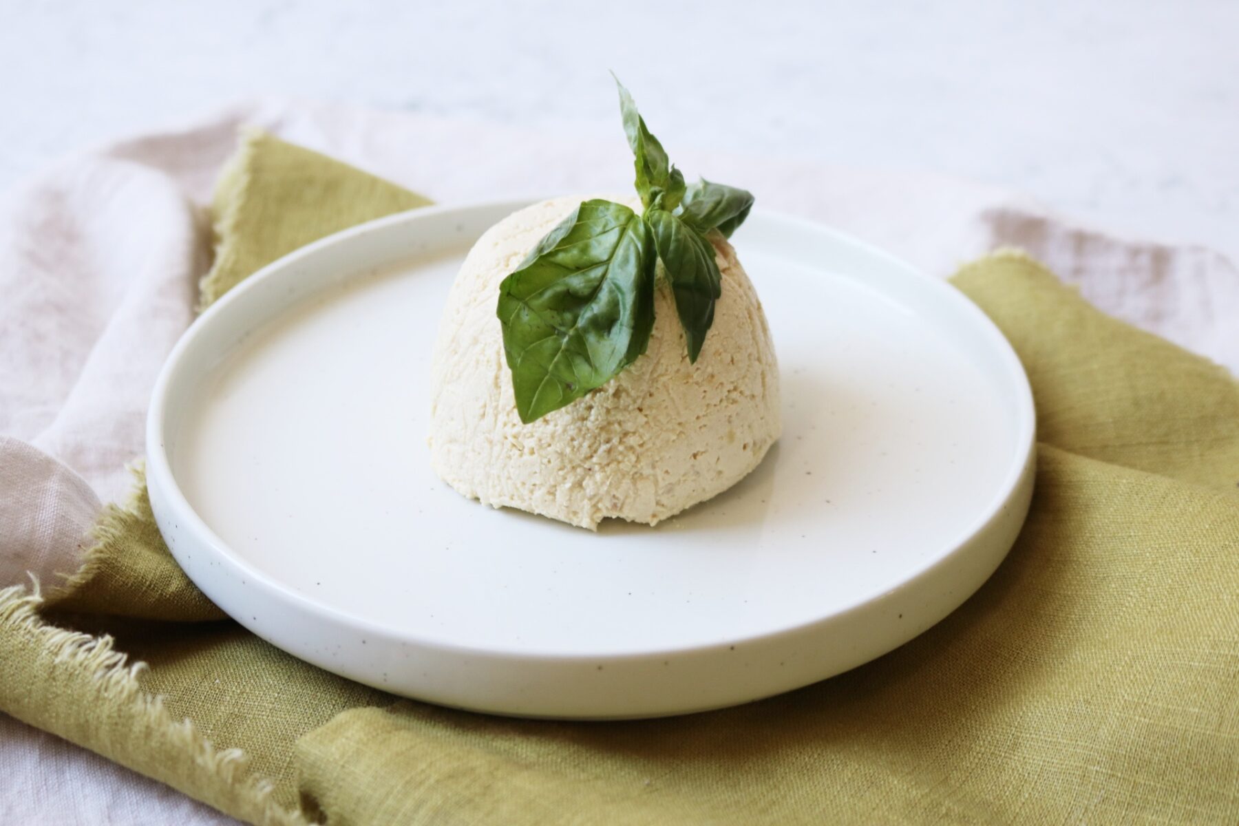 A dome of vegan ricotta on a plate topped with fresh basil