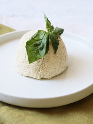 Vegan ricotta dome on a plate topped with fresh basil leaves