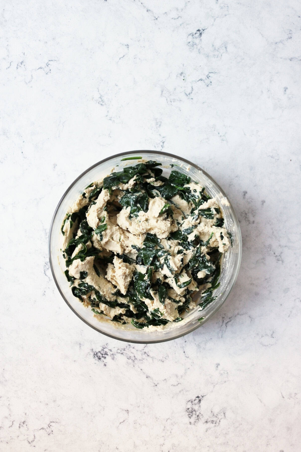 A glass mixing bowl filled with vegan ricotta and spinach