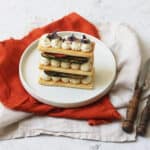 A Vegan Grilled Vegetable Mille-Feuille topped with micro herbs, on a plate with an orange napkin