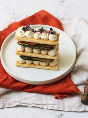 A Vegan Grilled Vegetable Mille-Feuille topped with micro herbs, on a plate with an orange napkin