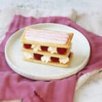 A Vegan Raspberry and Cream Mille-Feuille on a white plate with a pink napkin
