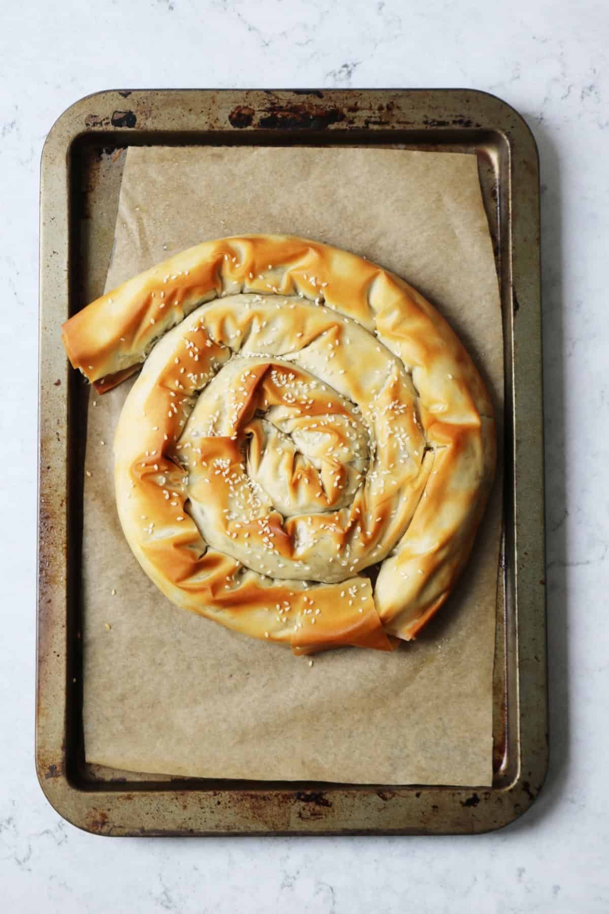 A baked vegan spiral spanakopita on a baking tray that is lined with brown baking paper