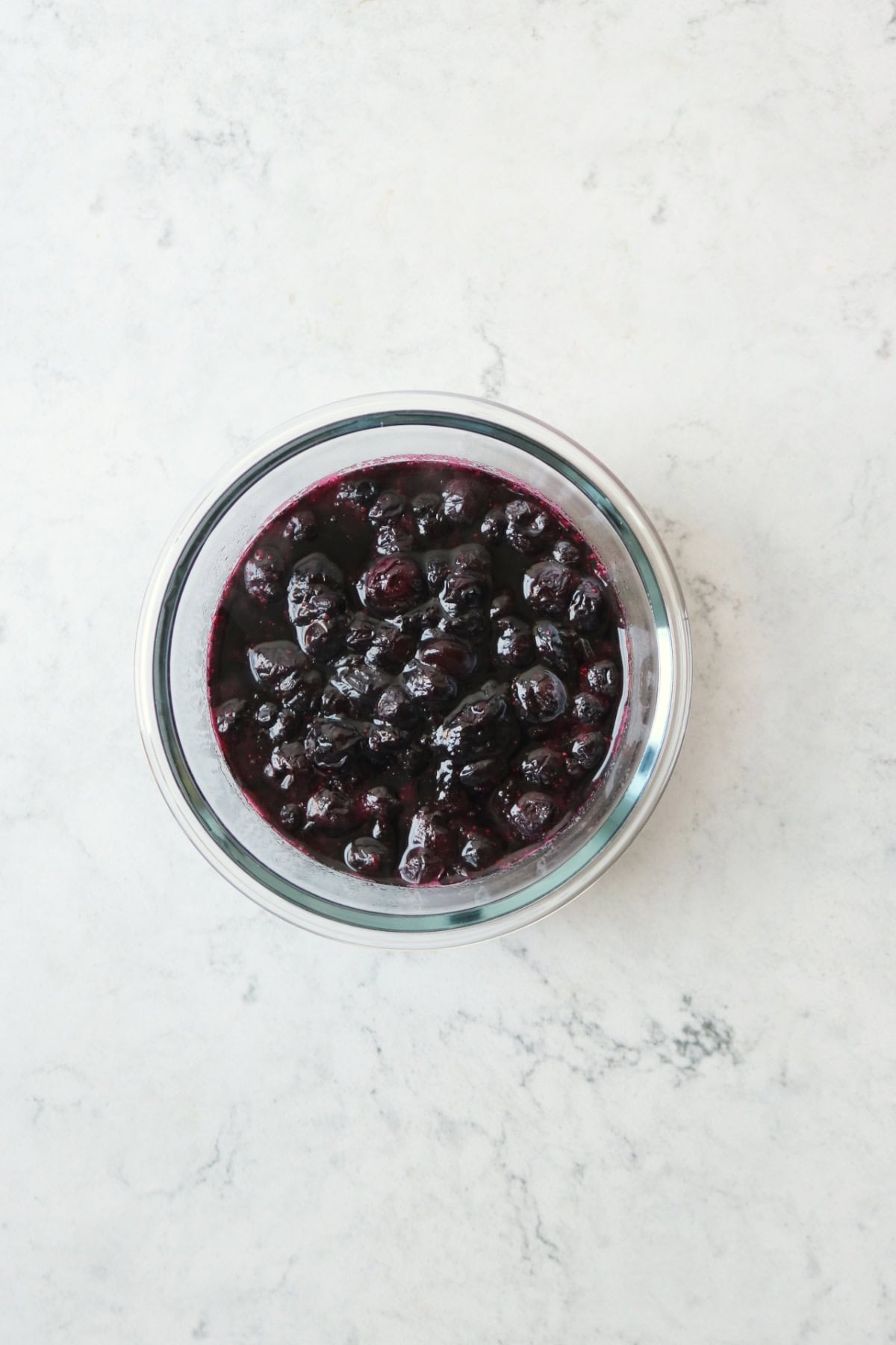 Blueberry compote in a glass bowl on a white marble counter top