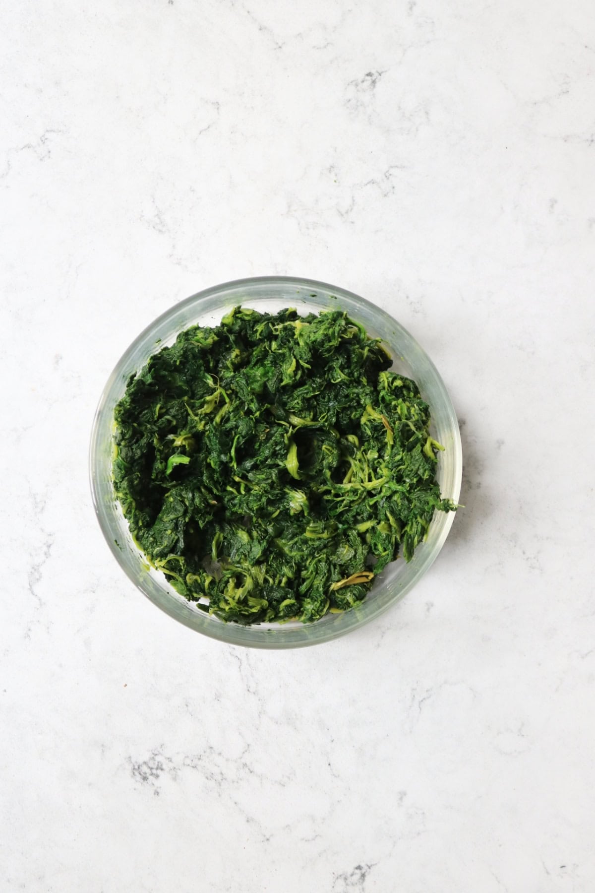 A glass bowl of chopped spinach with the moisture squeezed out