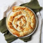 A baked Vegan Spiral Spanakopita on a plate on top of green and white napkins on a white marble counter top