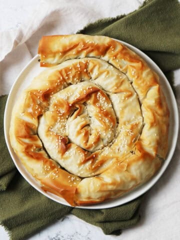 A baked Vegan Spiral Spanakopita on a plate on top of green and white napkins on a white marble counter top