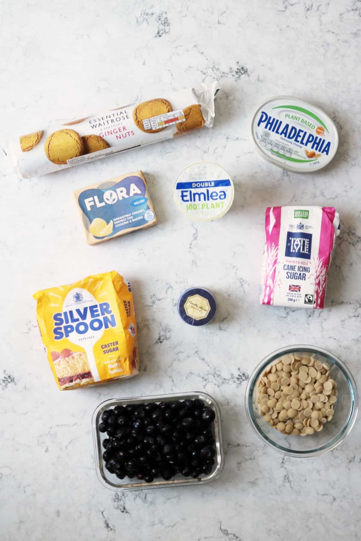 Ginger biscuits, vegan cream cheese, vegan butter, vegan cream, caster sugar, vanilla paste, icing sugar, blueberries and vegan white chocolate on a white marble counter top