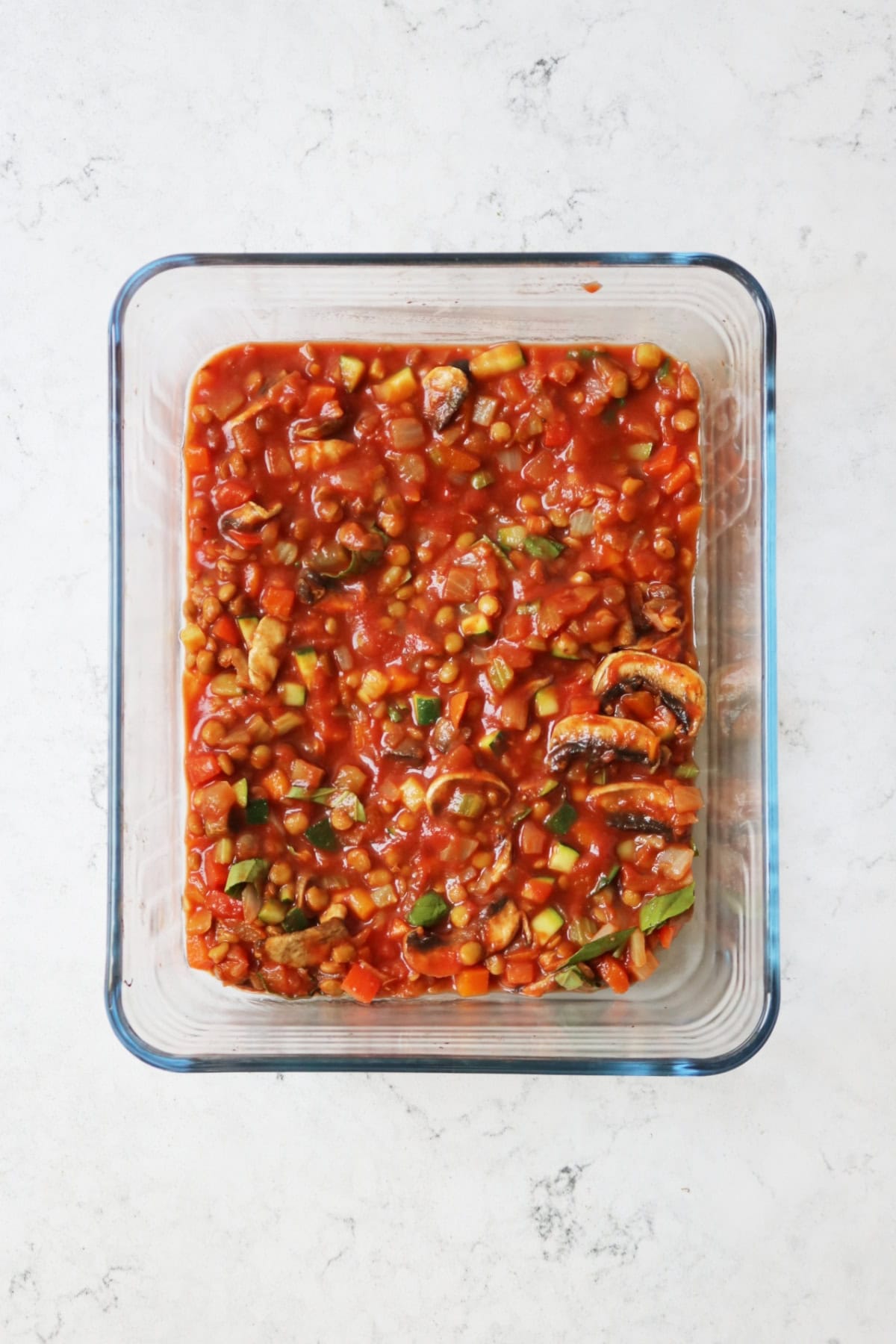 Tomato sauce in a glass oven dish on a white marble counter top