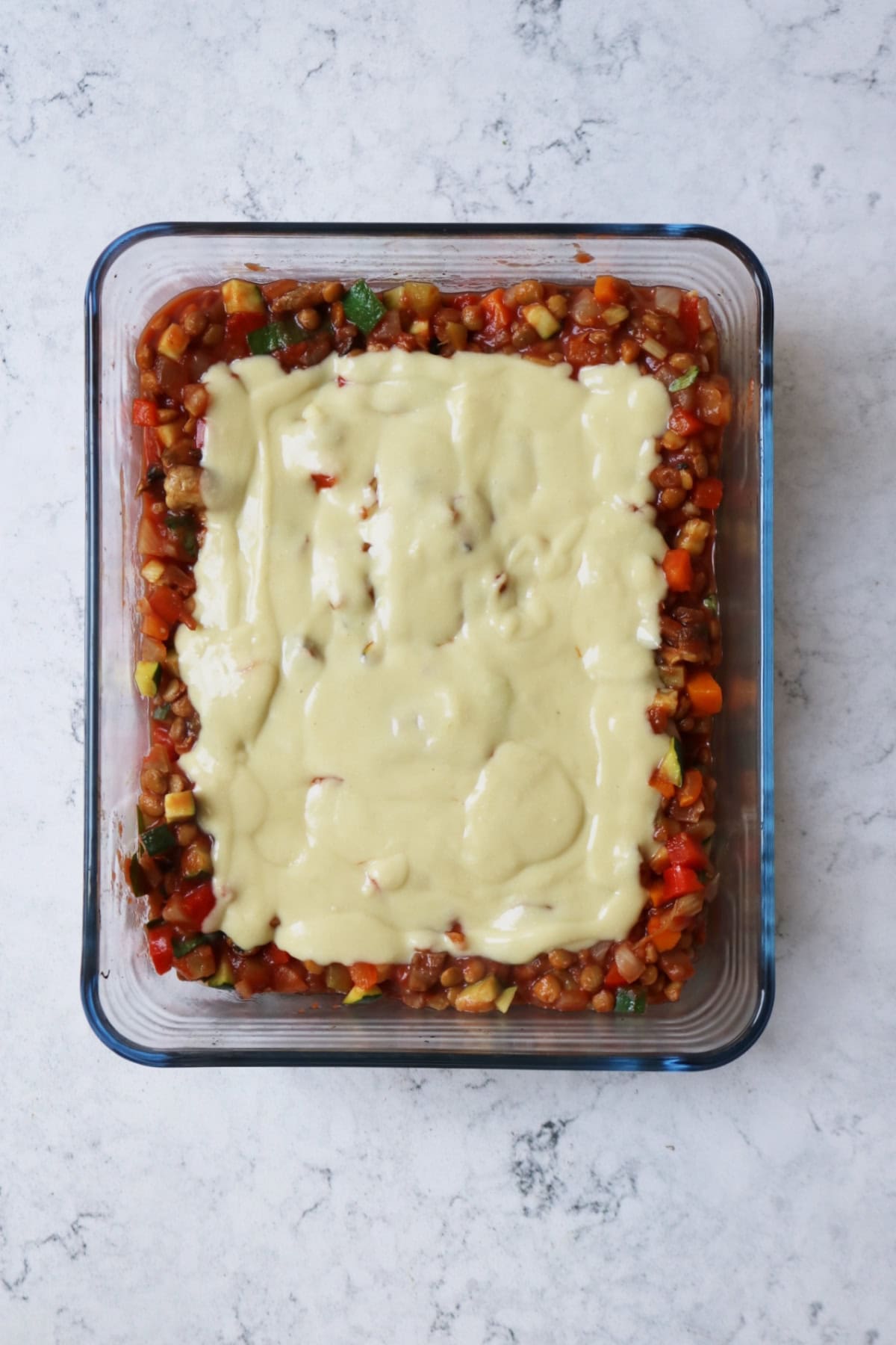 A glass oven dish filled with a layer of tomato sauce and a layer of vegan bechamel sauce