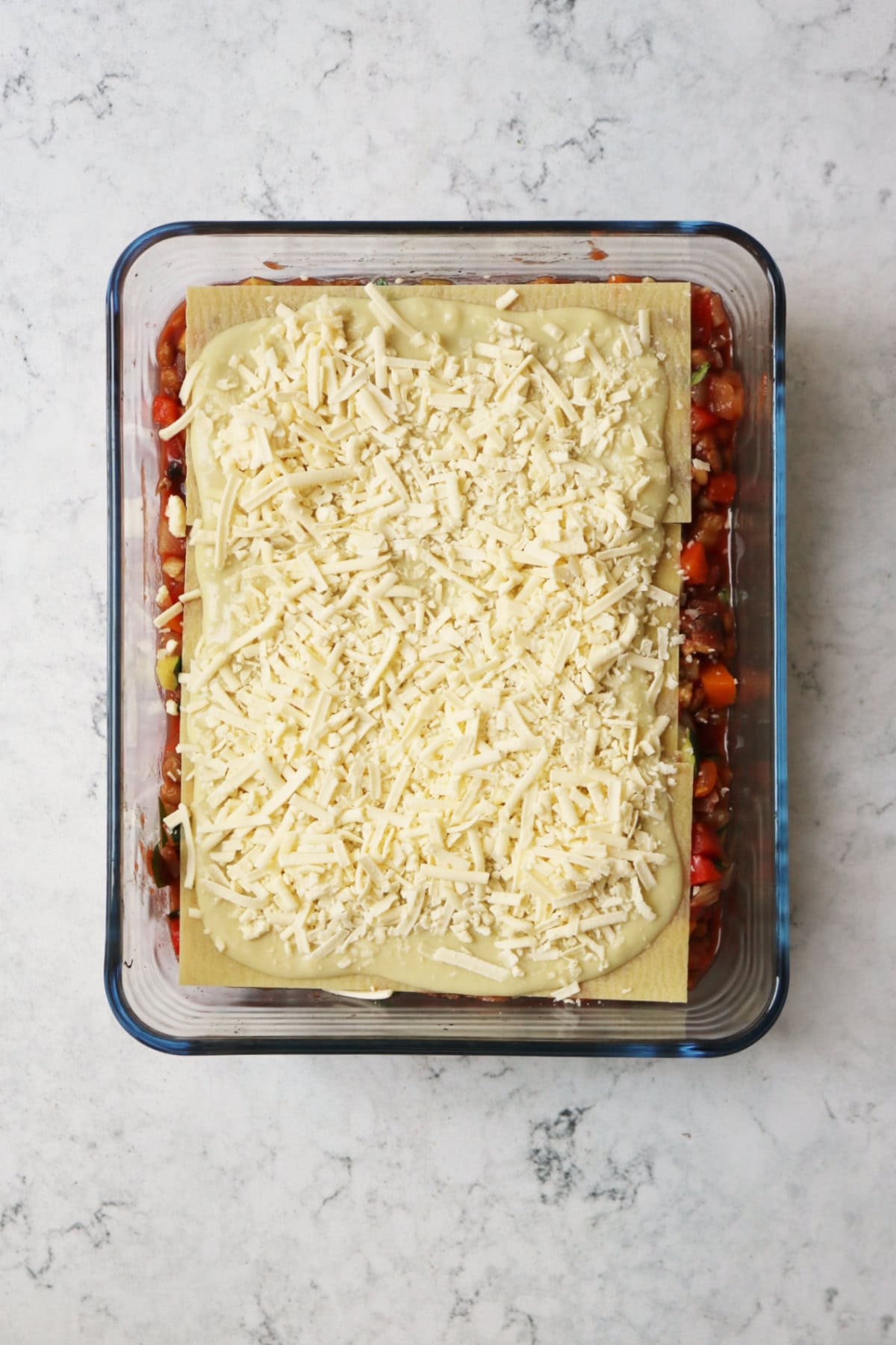 Uncooked vegan lentil lasagne in a glass oven dish on a white marble counter top