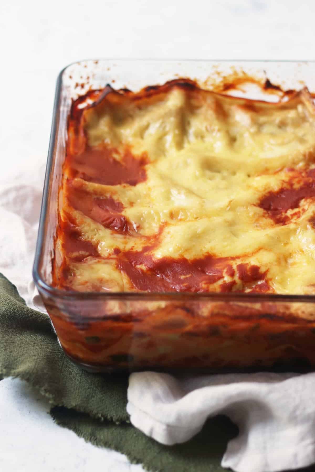 Baked vegan lentil lasagne in a glass oven dish on top of green and cream napkins.