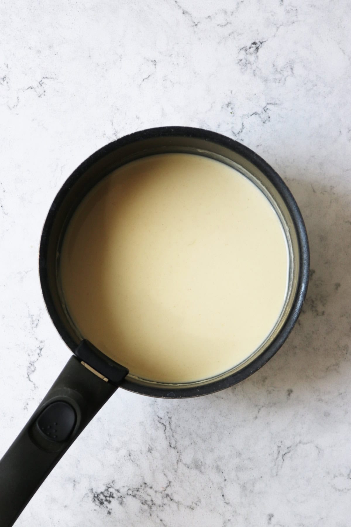 Vegan bechamel sauce in a sauce pan on a white marble counter top