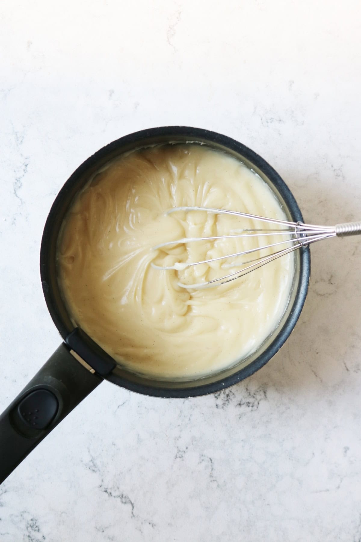 A saucepan full of creme patissiere and a metal whisk