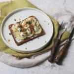 A plate topped with Kartoffelmad a type of Danish open-faced sandwich made of rye bread, potato slices, vegan creme fraiche, fried onions and chives.