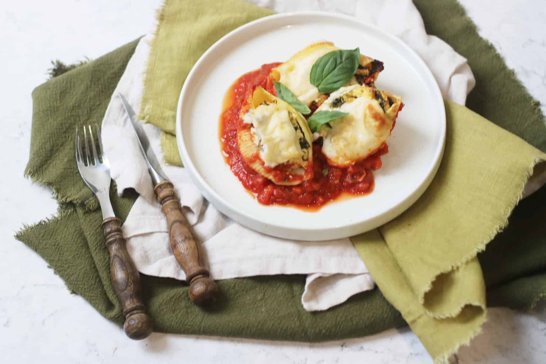 Vegan Spinach and Ricotta Stuffed Pasta Shells on a white plate with green napkins and a knife and fork