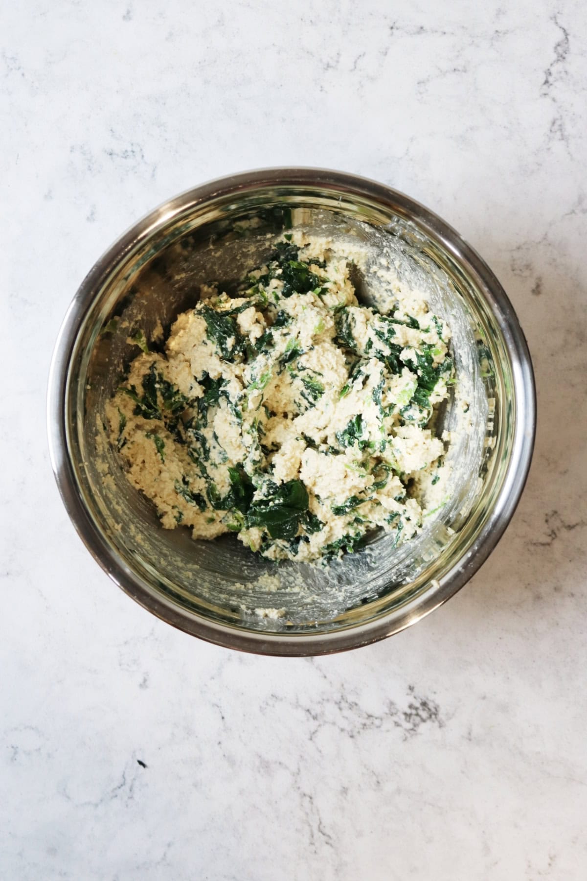 Vegan ricotta and spinach mixed in a metal mixing bowl