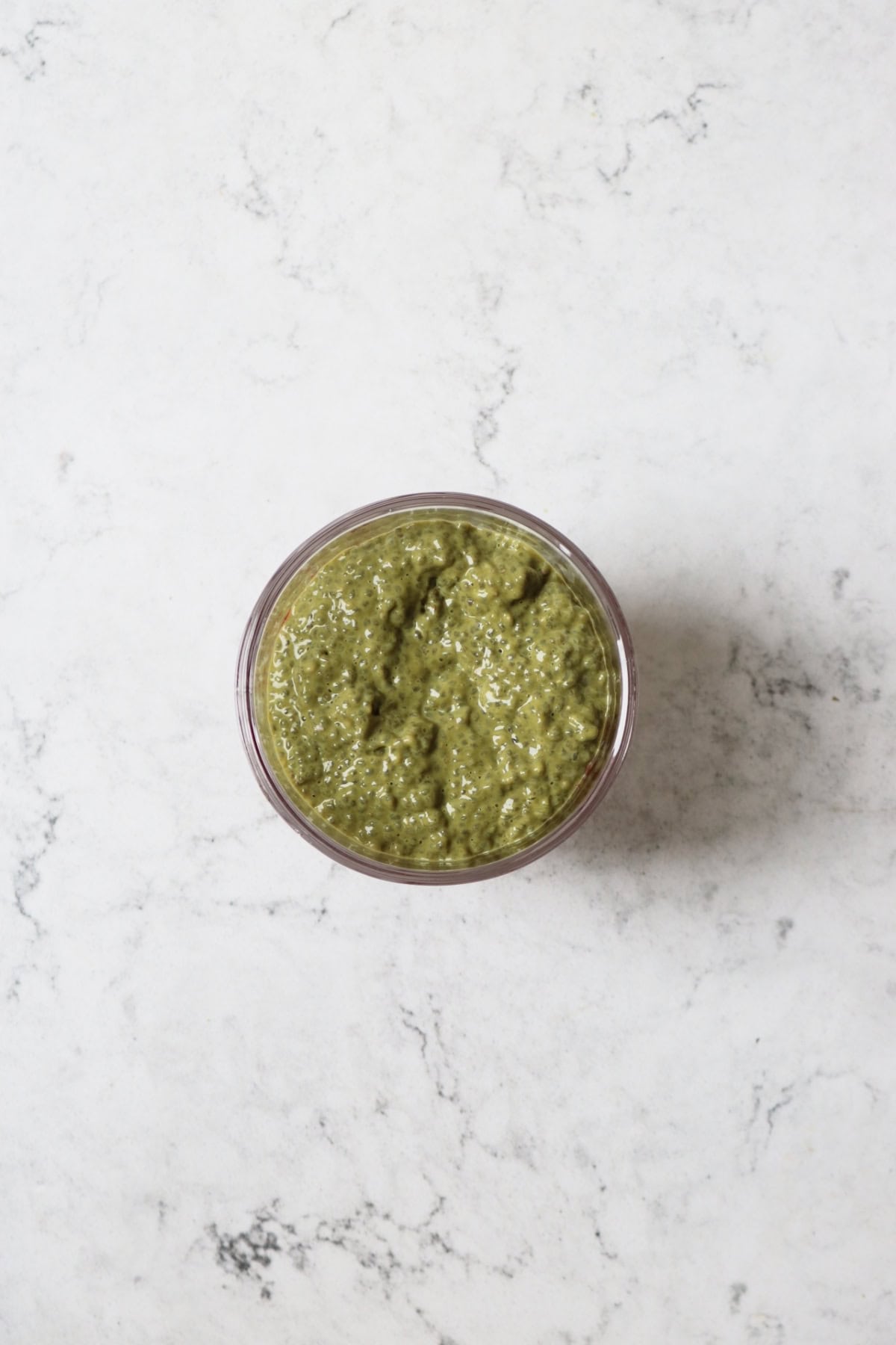 A layer of matcha chia pudding on top of mashed raspberries in a glass pudding bowl