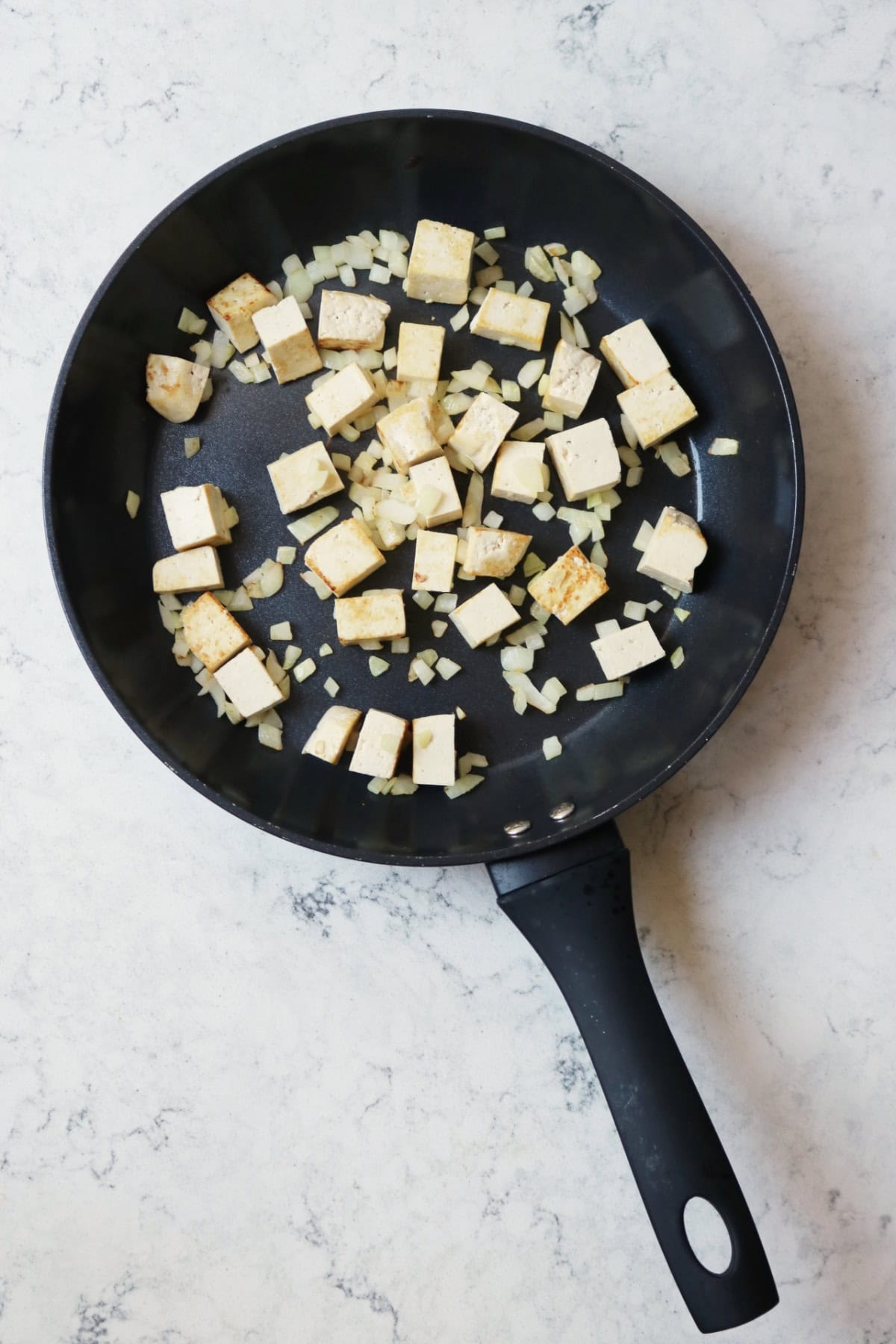 Frying onions and tofu in a large frying pan