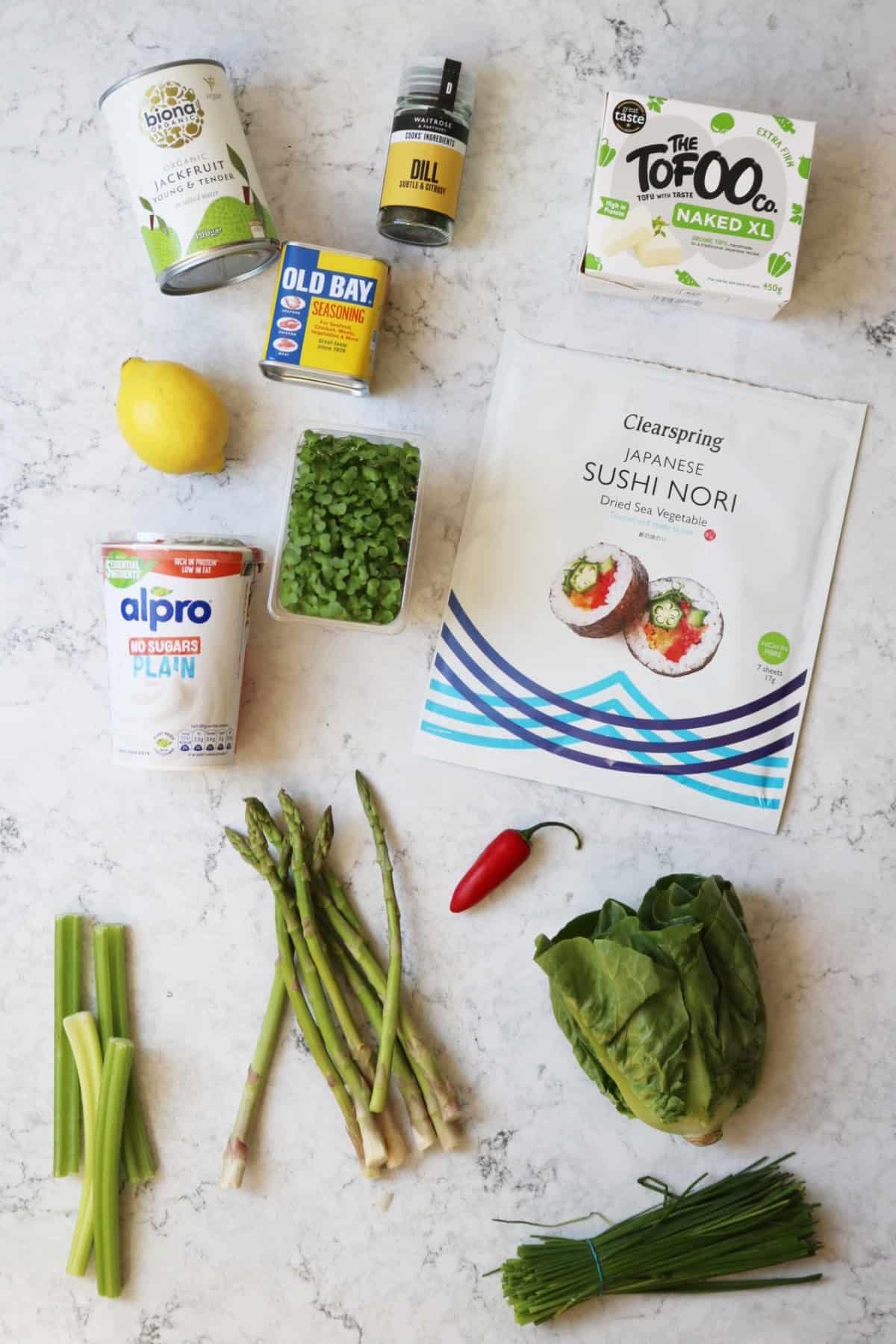 Tinned jackfruit, dill, tofu, lemon, old bay seasoning, vegan yogurt, cress, nori sheets, celery, asparagus, red chilli, gem lettuce, chives on a white marble counter top