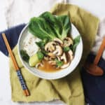 A bowl of Vegan Pho topped with pak choi, mushrooms, fresh herbs and a wedge of lime