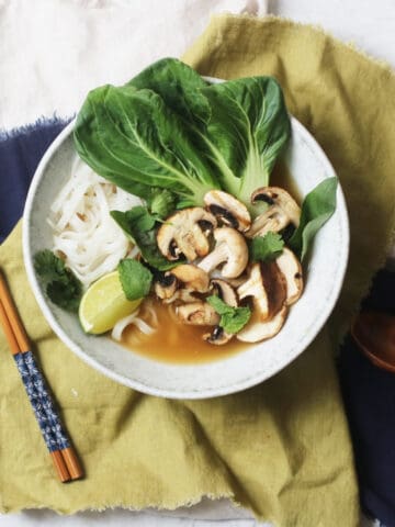 A bowl of Vegan Pho topped with pak choi, mushrooms, fresh herbs and a wedge of lime