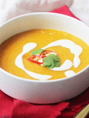 Vegan Carrot and Ginger Soup in a white bowl, served with a drizzle of yogurt, red chilli and coriander