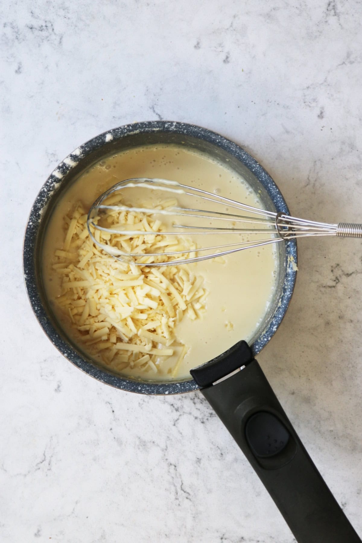 Adding vegan cheese to vegan bechamel sauce in a saucepan with a whisk
