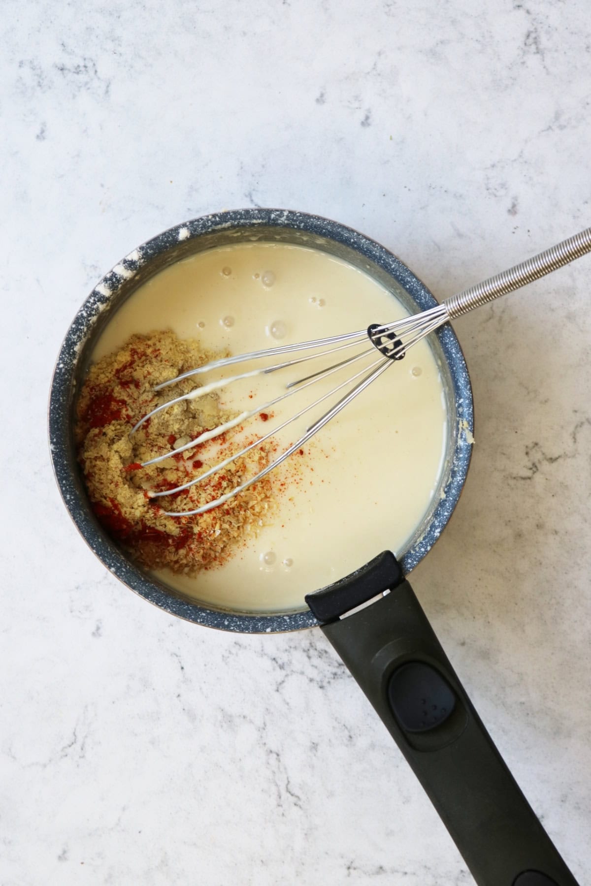 Adding seasonings to vegan cheese sauce in a saucepan with a whisk