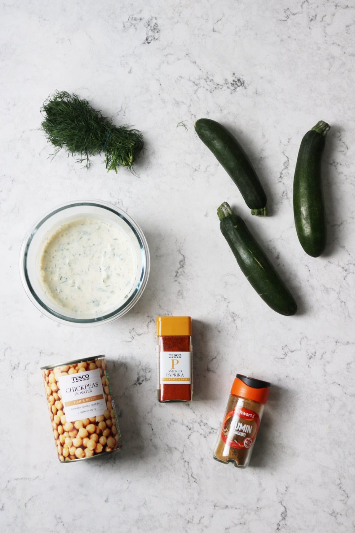 Dill, baby courgettes, vegan tzatziki, chickpeas, smoked paprika and cumin on a white marble counter top
