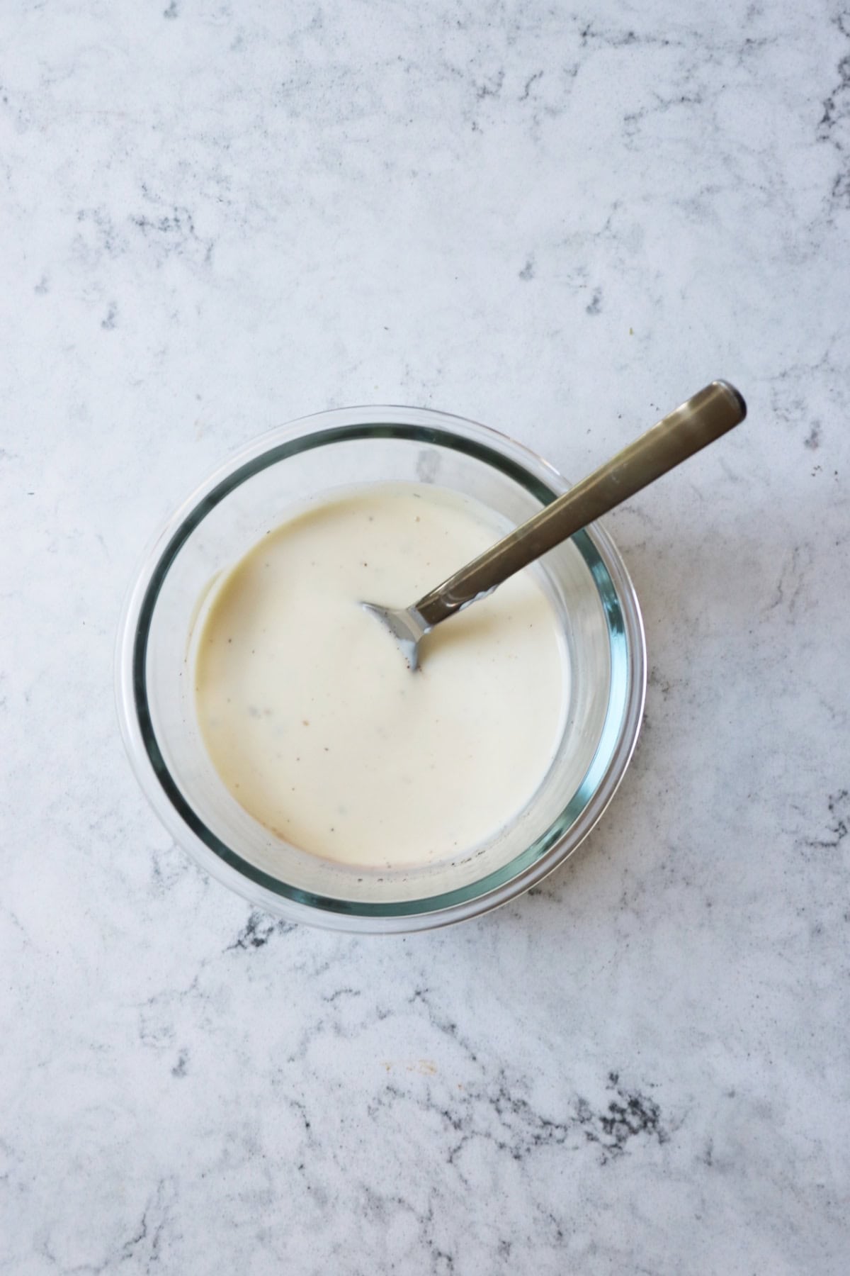 Vegan yogurt, red wine vinegar, garlic, salt and pepper mixed in a glass bowl