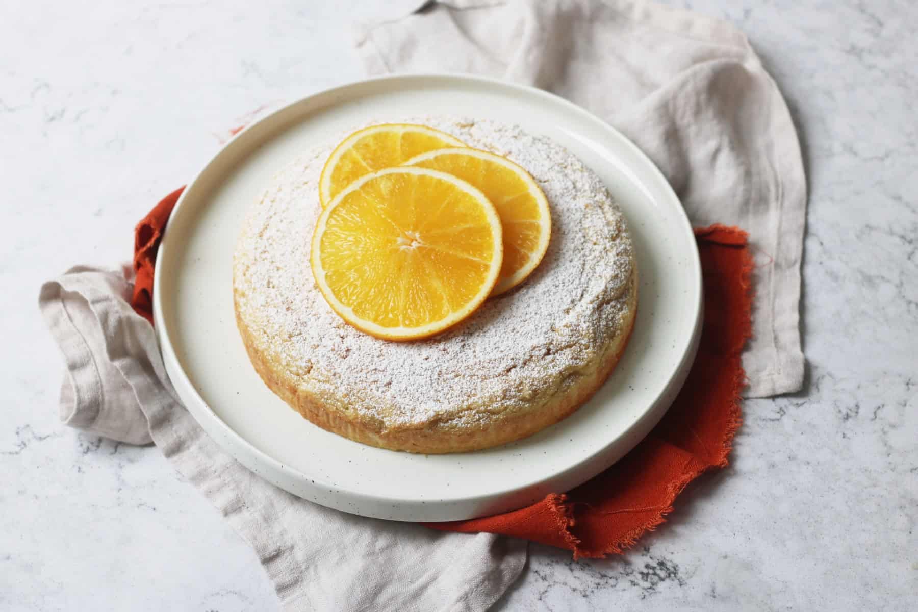 Plant Based Orange Polenta Cake topped with icing sugar and orange slices