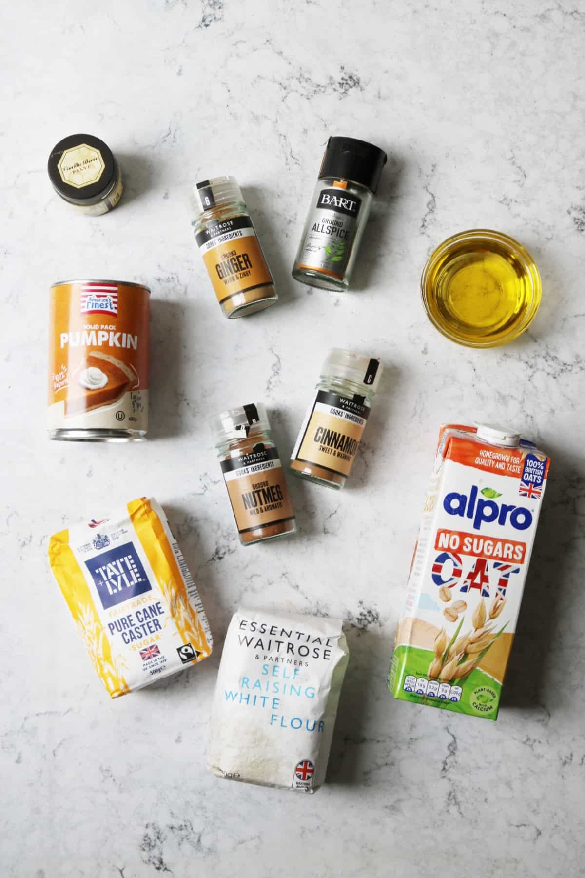 Vanilla bean paste, ginger, all spice, pumpkin puree, vegetable oil, caster sugar, cinnamon, nutmeg, oat milk, self raising flour on a white marble counter top